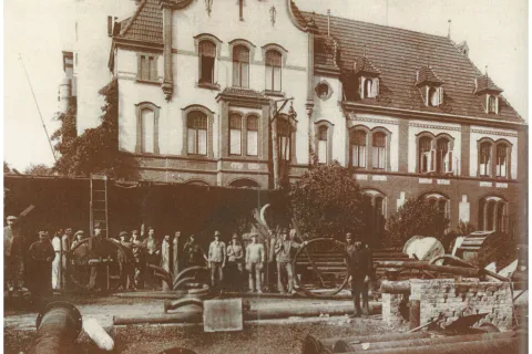 Schwarz-Weiß-Foto von 1924 mit den Arbeitern und Teilen der Fernwärmerohrleitungen vor dem Städtischen Elektrizitätswerk.