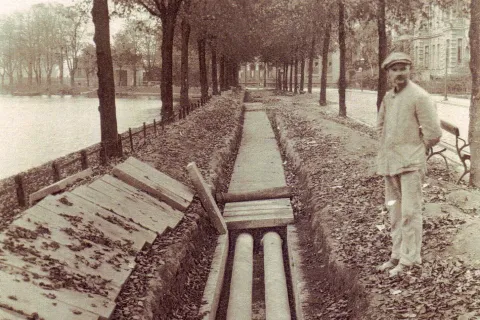 Schwarz-Weiß-Foto der August-Bebel-Straße. Der Fußgängerweg ist aufgegraben. Daneben steht ein Arbeiter.