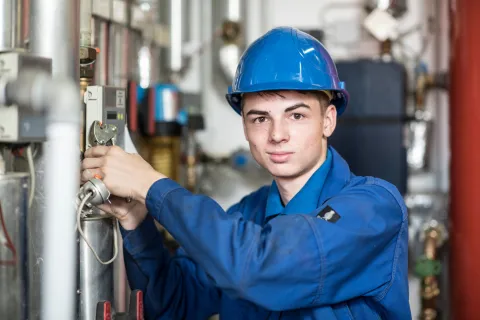 Ein Auszubildender in blauer Arbeitskleidung steht in einer Maschinenhalle.