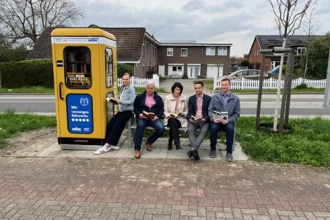 Personen sitzen lesend auf einer Bank neben einer Büchertauschbox.