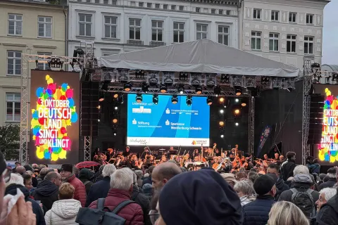 Menschen stehen vor einer Bühne und singen gemeinsam.