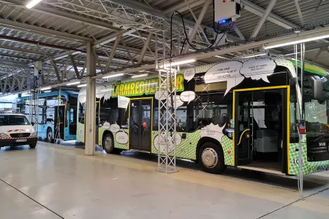 Bunt bedruckter Elektrobus in einer Halle des Nahverkehr Schwerins, dahinter steht ein blauer Bus.