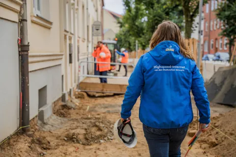 Eine Frau in blauer Arbeitsjacke läuft über eine Baustelle.