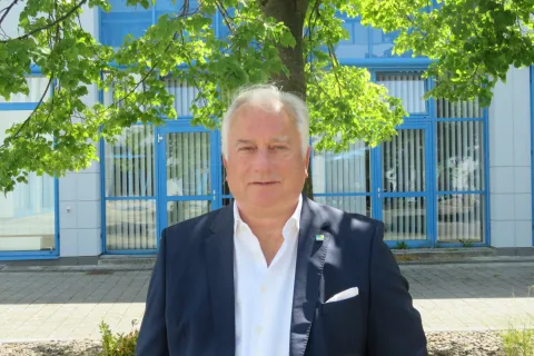 Der Geschäftsführer der Stadtwerke Schwerin Dr. Josef Wolf steht unter einem Laubbaum vor dem Stadtwerkehauptgebäude.