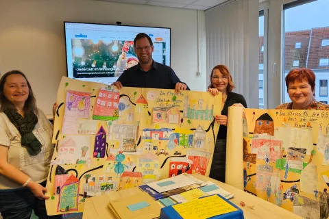 Vier Personen stehen in einem Büro uns halten Kinderbilder in die Kamera.