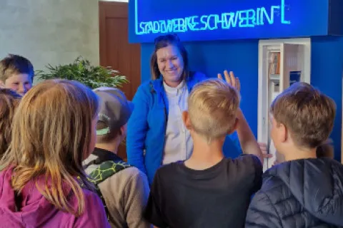 Eine Gruppe Schüler mit einer Stadtwerkemitarbeiterin am Medienschrank.