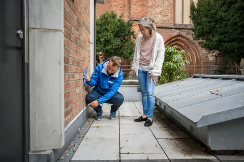 Ein Mitarbeiter der Stadtwerke Schwerin misst mit einem Zollstock an der Hauswand.