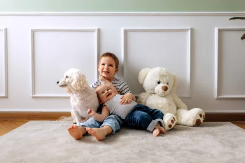 Zwei Kinder sitzen mit nackten Füßen auf dem Fußboden und lachen.