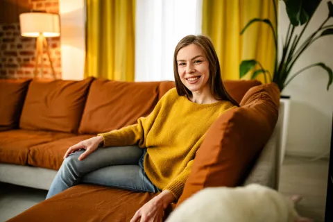 Eine Frau sitzt gemütlich auf dem Sofa und lächelt.