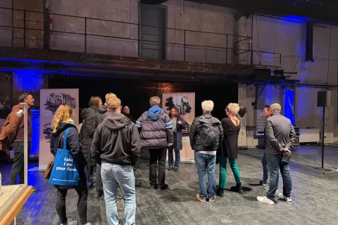 Eine Besuchergruppe steht in einer alten Werkshalle.