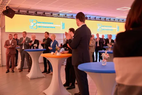 Eine Gruppe von Menschen steht in einem festlich beleuchtetem Raum und applaudiert.