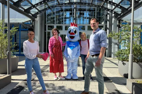 Vier Personen stehen mit dem Stadtwerke Maskottchen vor dem Hauptsitz der Stadtwerke Schwerin.