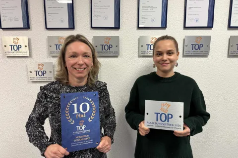 Zwei Frauen halten die Auszeichnungsplaketten zum in den Händen.