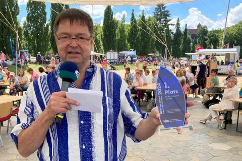 Moderator Leif Tennemann hält den Pokal für den NDR Chorcontest in den Händen
