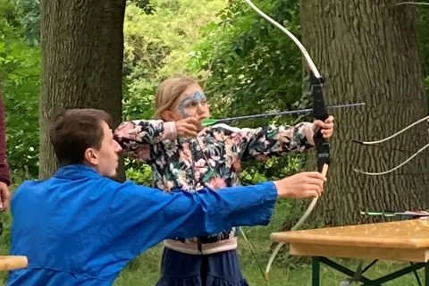 Ein Mädchen spannt einen Bogen und wird von meinem Herren unterwiesen.