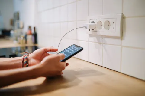 Eine Person tippt auf einem Handy. Das Handy ist an eine Steckdose angeschlossen.