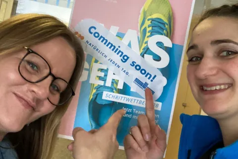 Zwei Frauen stehen vor einem Plakat zum Schrittwettbewerb.