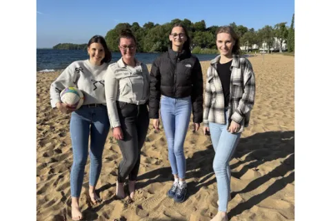 Vier junge Frauen am Strand mit einem Beachvolleyball