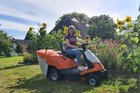 Frau sitzt auf einem Rasenmäher im Garten