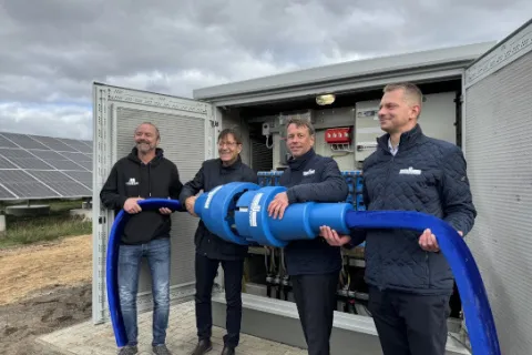 Vier Männer stehen vor einem Trafoschrank und halten einen großen Stromstecker