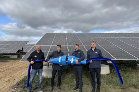 Vier Männer stehen vor PV-Modulen und halten einen großen Stromstecker in den Händen