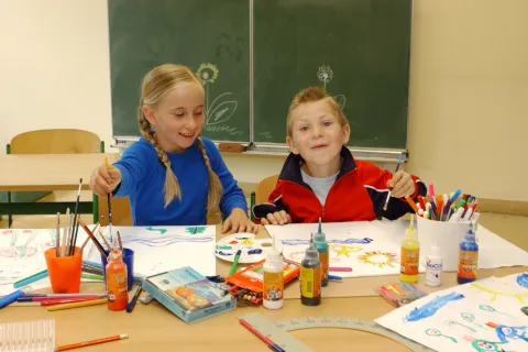 Ein Mädchen und ein Junge sitzen vor einer tafel und malen Bilder