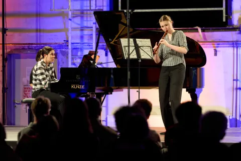 Eine Pianistin und eine Flötenspielering stehen auf einer Bühne.