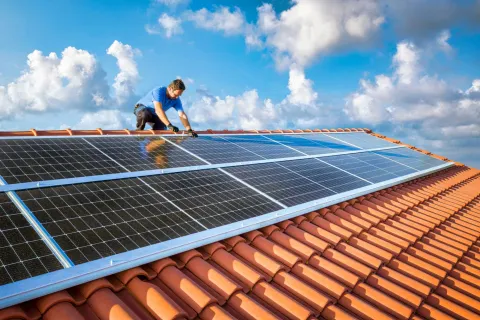 Ein Handwerker installiert eine Photovoltaikanlage auf einem Dach.