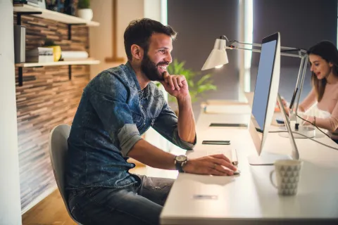 Ein Mann sitzt lächelnd vor einem PC.