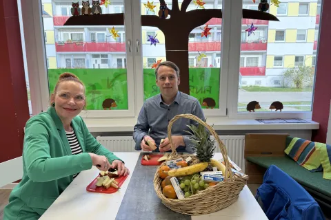 Eine Frau und ein Mann sitzen an einem Tisch und schneiden Obst.