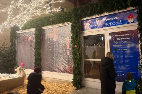 Ein kleine Familie schaut sich die Programmübersicht am Stadtwerke Märchenzelt auf dem Schweriner Weihnachtsmarkt an.