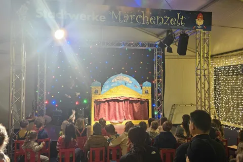 Blick auf eine Bühne mit Puppentheater. Davor sitzt Publikum.