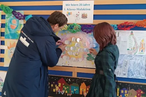 Ein Mann und eine Frau bestaunen bunte Kinderzeichnungenan einer Wand