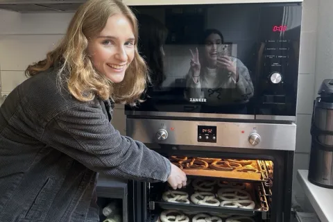 Eine junge Frau steht an einem Backofen und holt Brezel heraus