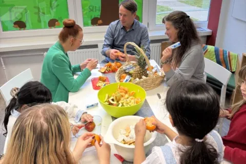 Kinder und Erwachsene sitzen an einem Tisch und schneiden gemeinsam Obst