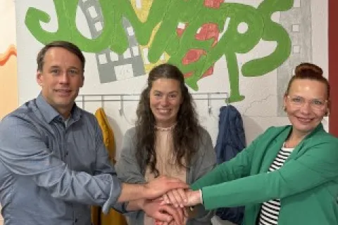 Zwei Frauen und ein Mann legen symbolisch die Hände aufeinander