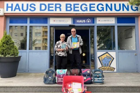 Ein Mann und eine Frau stehen mit gespendeten Ranzen vor einem Haus