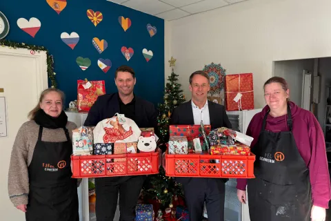 Vier Personen stehen mit bunt verpackten Weihnachtsgeschenken im Speiseraum der Kindertafel Schwerin