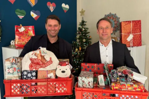 Zwei Männer stehen mit Geschenken vor einem Tannenbaum
