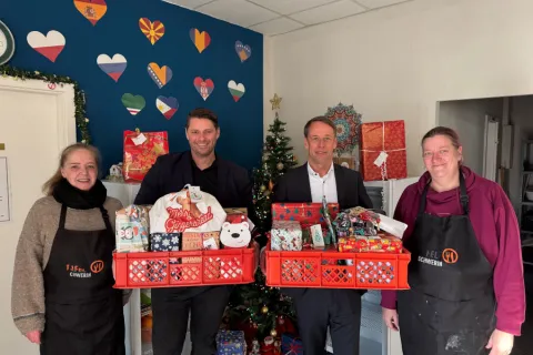 Zwei Männer und zwei Frauen stehen mit Geschenken vor einem Tannenbaum