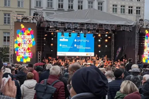 Vor einer großen Bühne auf einem Marktplatz stehen viele Menschen