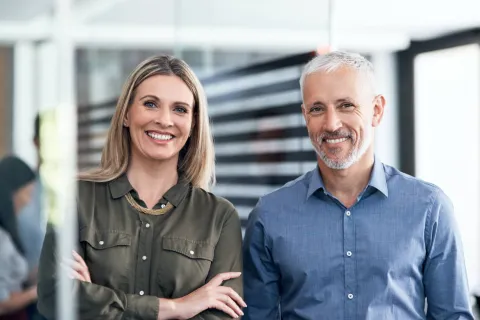 Ein Mann und eine Frau im Büro lächeln in die Kamera