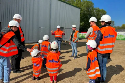 Gruppen mit Erwachsenen und Kleinkindern nehmen mit Warnwesten und Bauhelmen an einer Führung teil