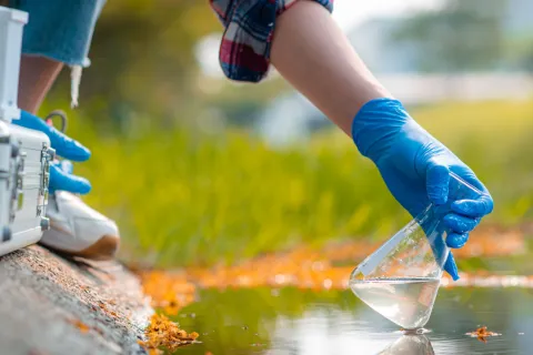 Hand eines Wissenschaftlers, der eine Wasserprobe aus einem See entnimmt