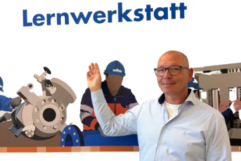 Ein gewerblicher Ausbildungsbetreuer steht vor einer gestalteten Wand