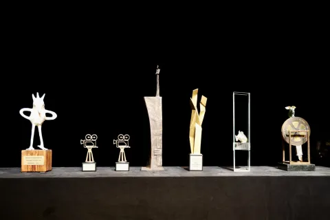 Sieben Trophäen der unterschiedlichen Kategorien des Filmkunstfestes MV stehen aufgereiht vor einem schwarzen Hintergrund.