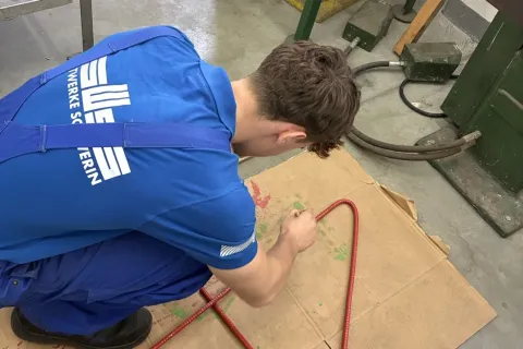 Ein gewerblicher Azubi lackiert eine Metallstange rot