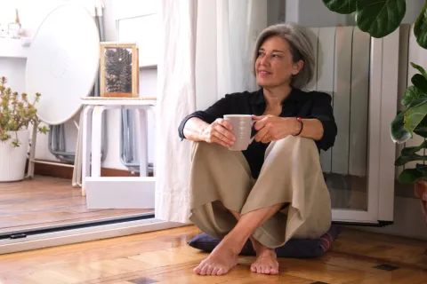 Eine Frau sitzt entspannt mit dem Rücken an einer Heizung und schaut nach draußen.