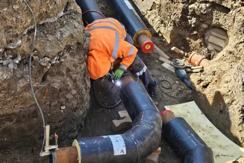 Ein Mann mit Arbeitsschutzbekleidung schweißt in einem Graben an einem großen schwarzen Rohr.