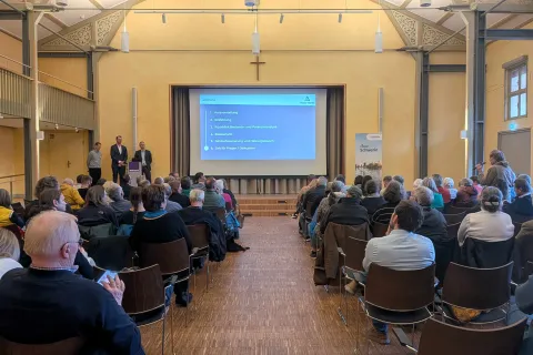 Menschen sitzen in einem Saal und schauen auf eine Präsentation
